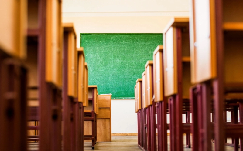 Rows of wooden desks leading towards a green chalkboard in a classroom.